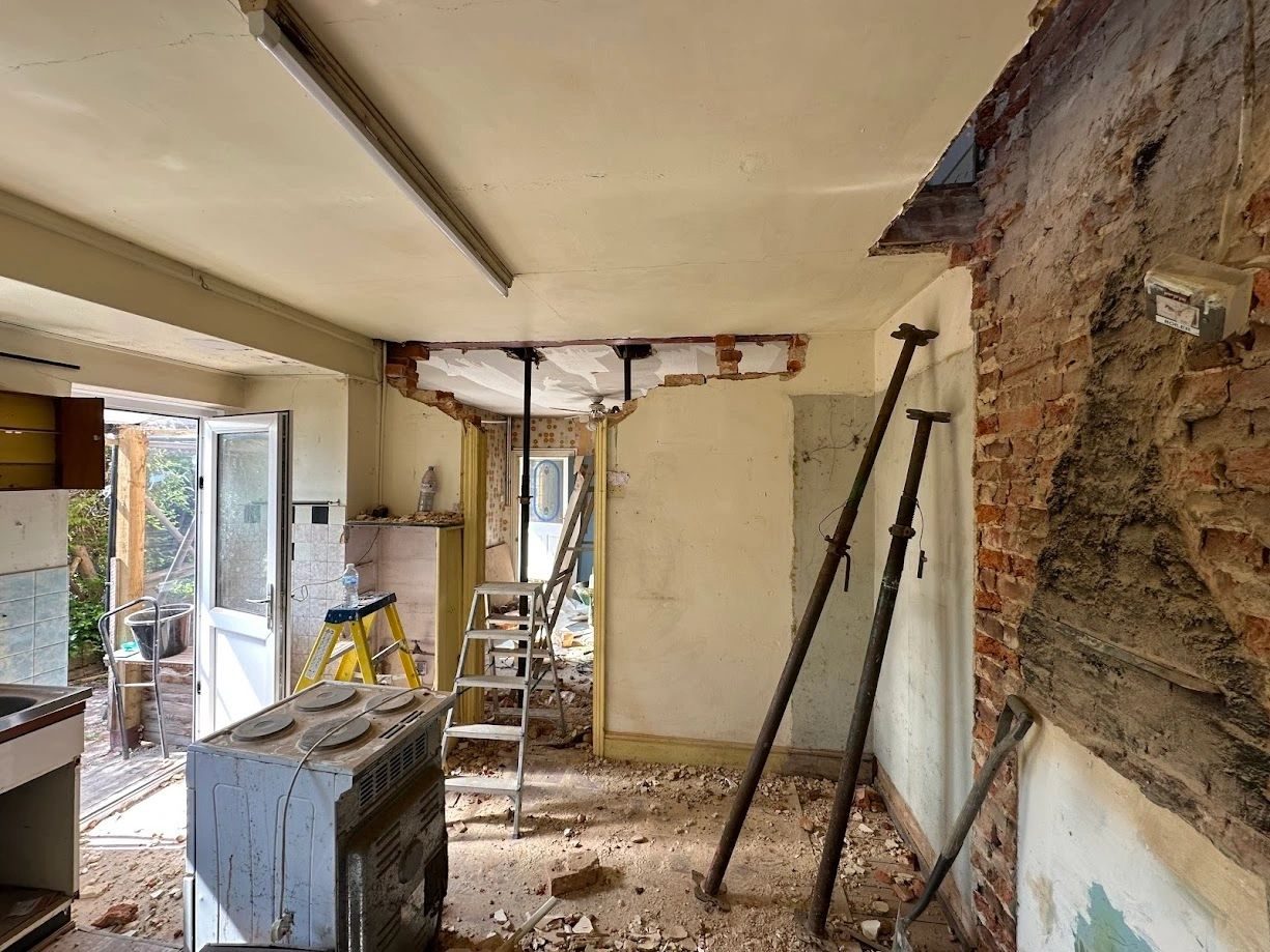 An old kitchen stripped out to bare brick and plaster, with props holding a new opening.